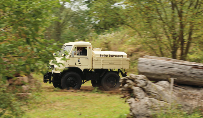 Eksploatowany w Berlinie przy oczyszczaniu miasta Unimog U 401 miał 25-konny silnik, generowane ciepło przenikało do wnętrza przez blachy kabiny nagrzewając ją niemiłosiernie; niewielkie jej rozmiary powodują, że kierowca musi się praktycznie wślizgnąć za kierownicę… Wejście do środka jest nieco kłopotliwe, oparcie dla stopy daje specjalna obręcz na feldze koła, nie ma żadnych uchwytów ani poręczy… Deska rozdzielcza oraz różne dźwignie wyglądają bardzo rustykalnie, ale są proste w obsłudze i jest ich niewielka ilość. Pedały są bardzo małe i leżą bardzo blisko siebie, pedał gazu jest wręcz mikroskopijny. Przyzwyczajenia wymaga obsługa niesynchronizowanej skrzyni biegów. Malutki U 401 niewiarygodnie sprawnie pokonuje drogę nieutwardzoną, nic się pod tym względem nie zmienia, gdy z drogi zjeżdżam na łąkę. Jadąc, mam uczucie, że to prawdziwy, trudny do pokonania król bezdroży… (fot. Mercedes-Benz)